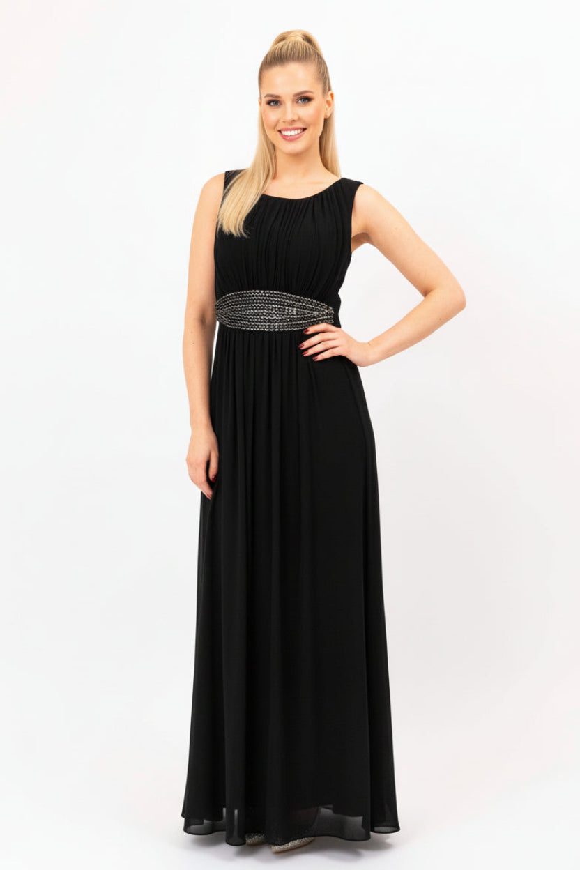 A woman wearing an elegant encrusted beaded black evening maxi dress with thin straps, full length, standing against a white background.