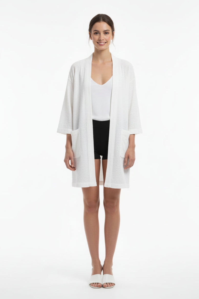 Woman wearing a white cardigan over a white top and black shorts on a white background
