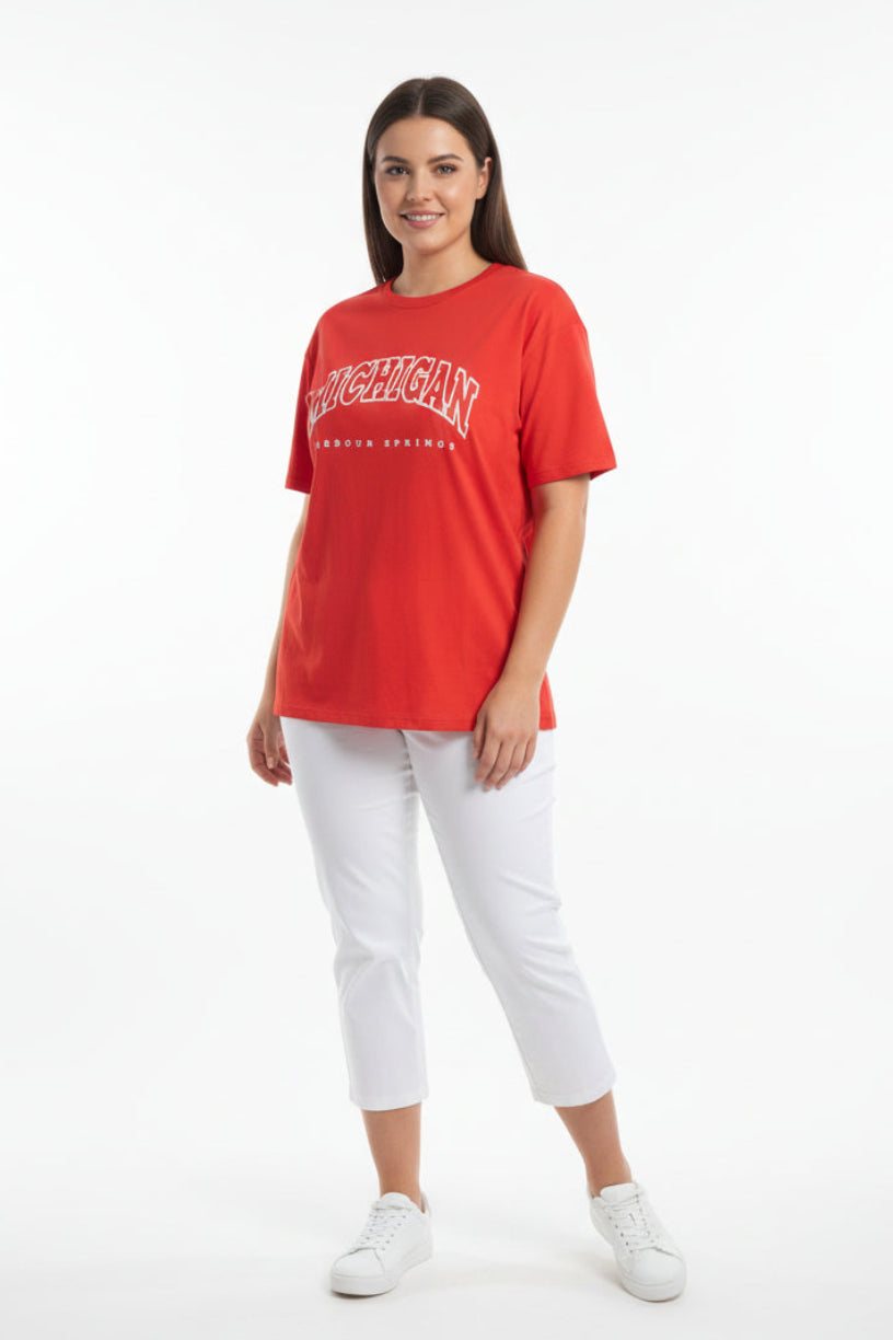 Woman wearing a red t-shirt with a logo and white pants on a white background