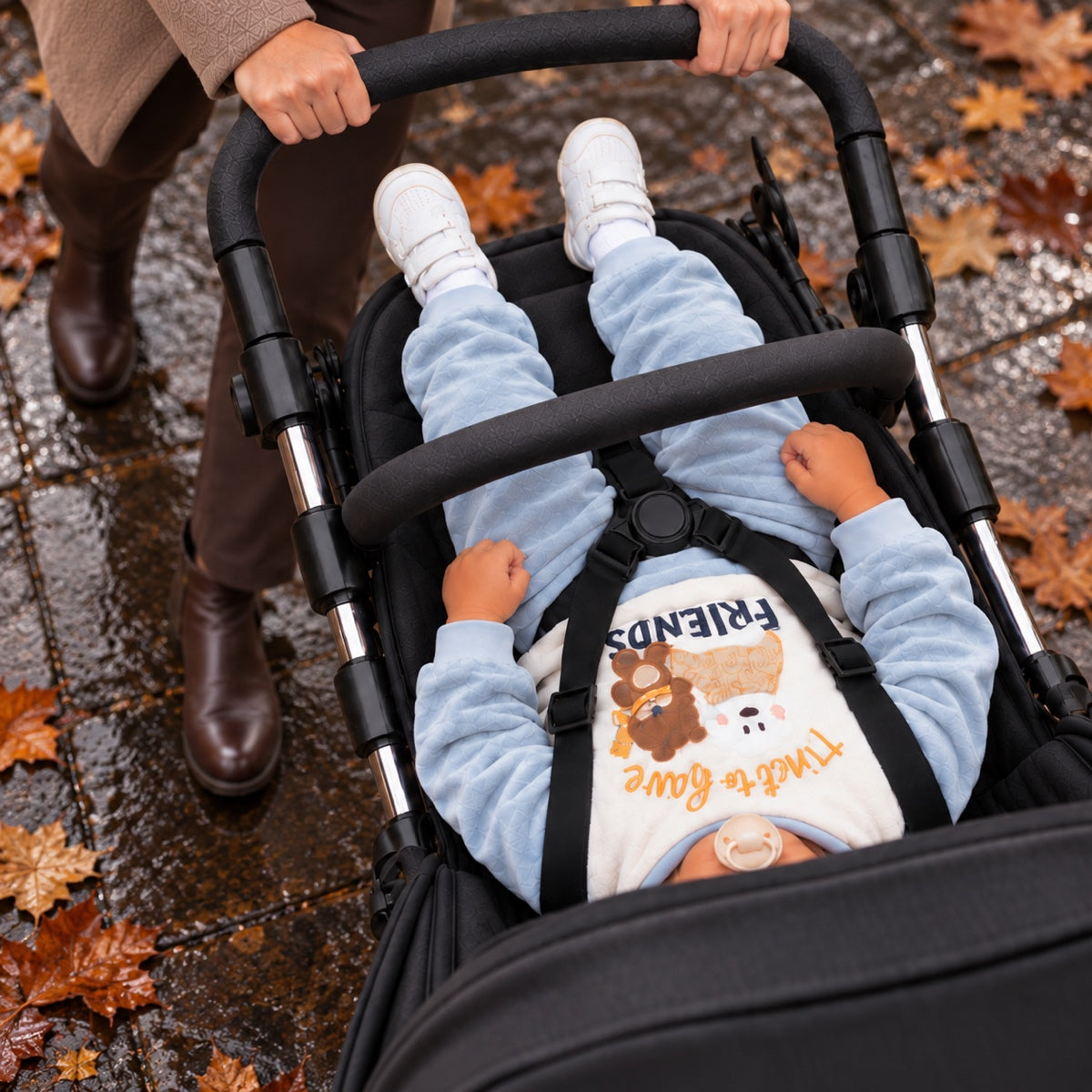 Toddler in a pushchair wearing a printed sweatshirt, seen from above among autumn leaves