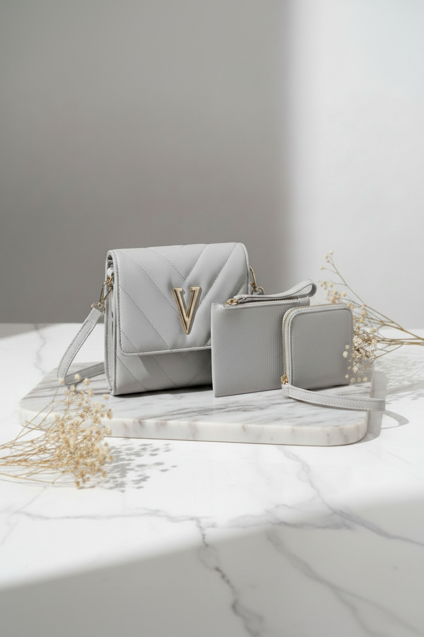A light gray quilted handbag set with a matching wallet and pouch, styled on a marble tray with dried flowers against a gray and white background.