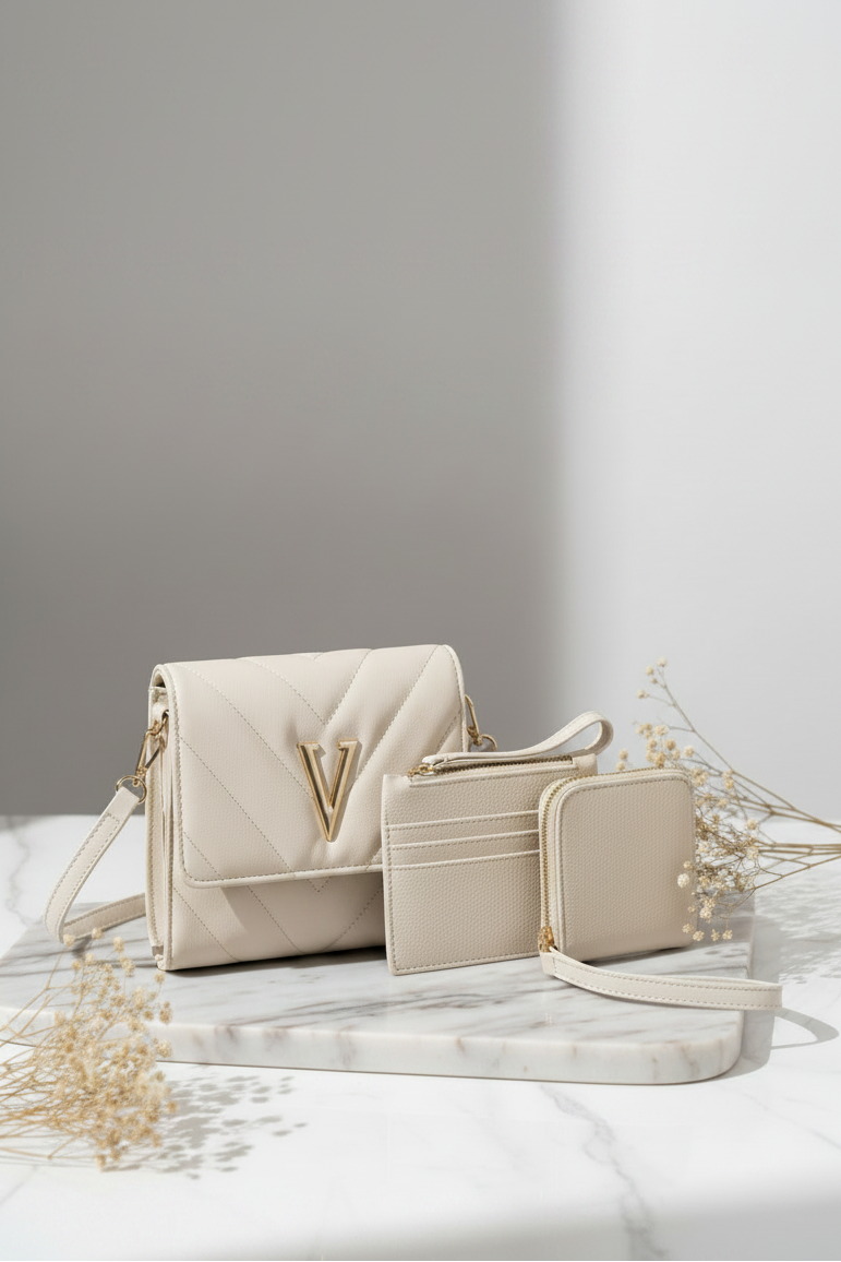 A cream-colored quilted leather handbag set with matching card holder and wallet, styled on a white marble tray with dried flowers against a gray background.