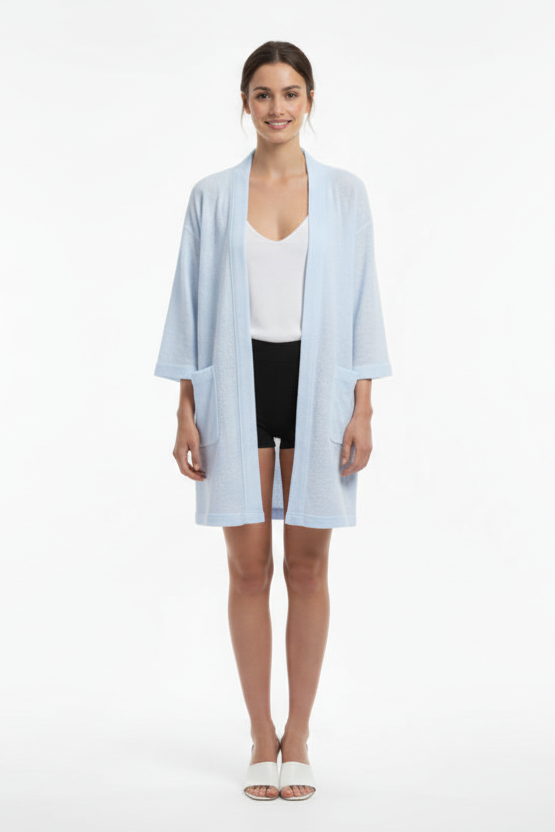 Woman wearing a light blue cardigan over a white top and black shorts on a white background