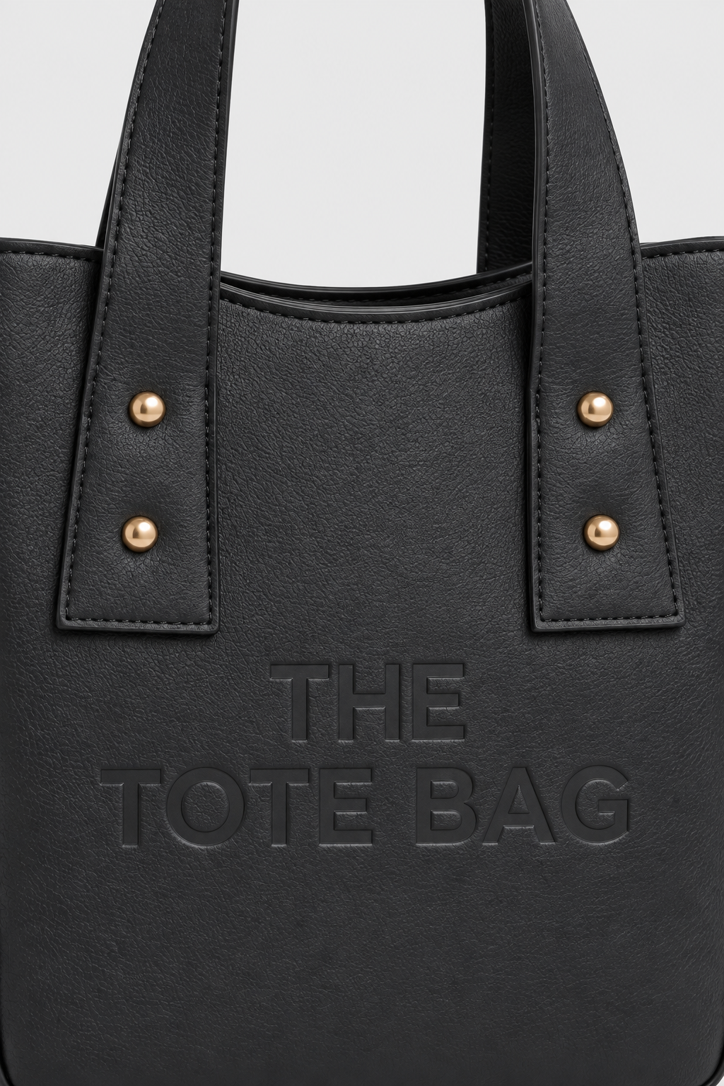 Close-up of black tote bag texture, embossed front design and gold-tone studs